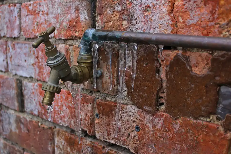 Outdoor faucet on a brick wall with icicles hanging from the pipe