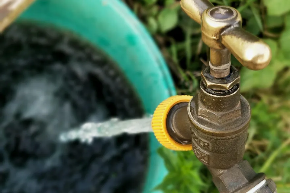 Brass outdoor tap with water running into a bucket