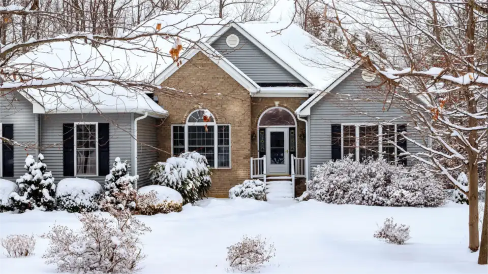 Brick and gray-sided house with snow covering the front yard and shrubs